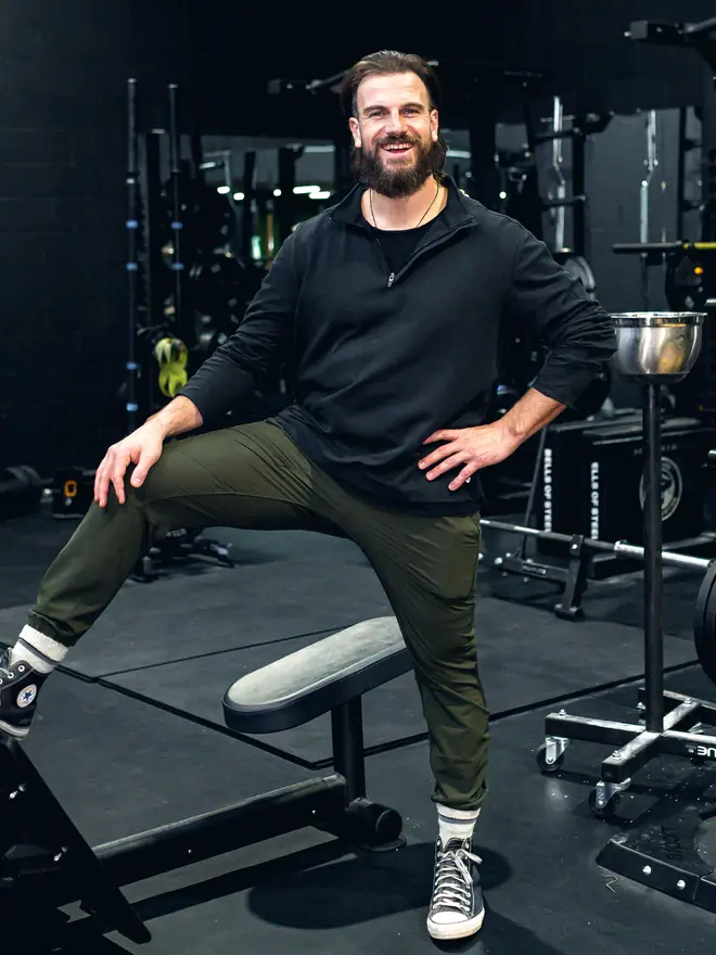 Aaron Buat resting a foot on a weight bench between sets, mid conversation.